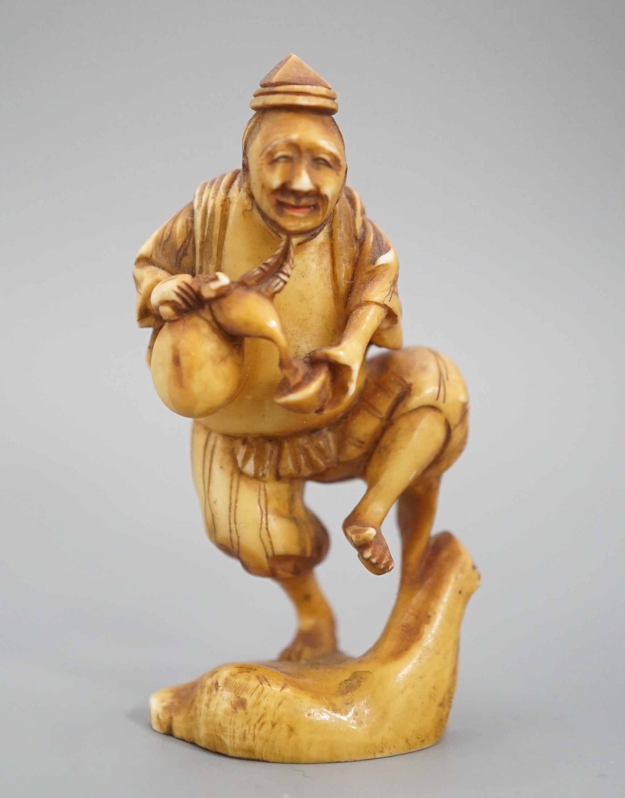 A Japanese ivory okimono of a man dancing and pouring wine from a flask, signed, Meiji period, 7cm